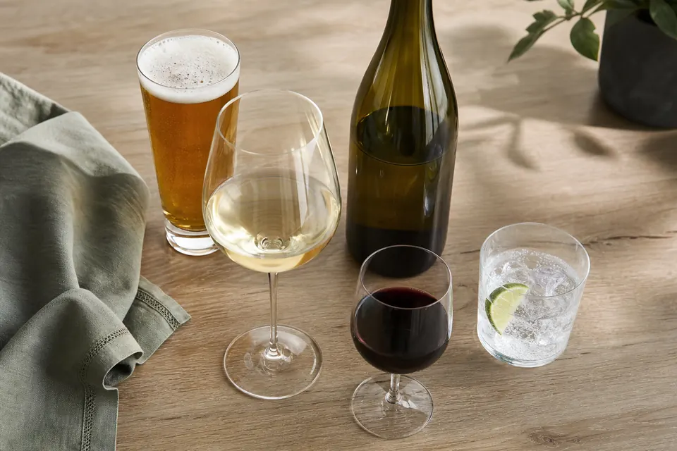 A pint of beer, a large glass of white wine, a small glass of red wine and a gin and tonic on a wooden table beside an unlabelled bottle.